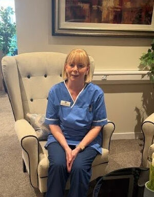carer in light blue nurses uniform sat in cream chair