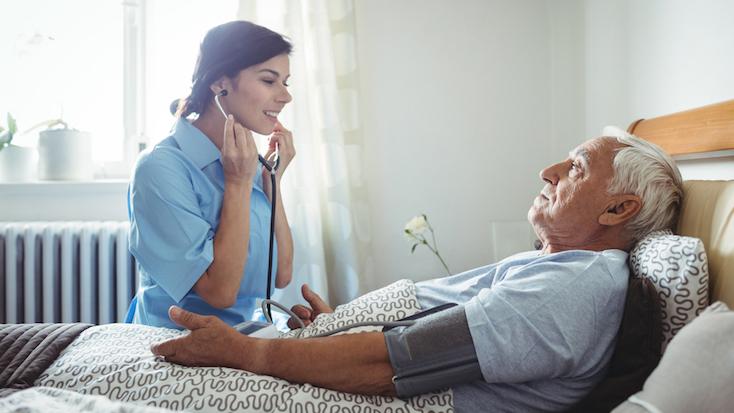 nurse caring for an elderly man in care home bed